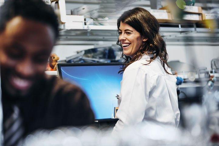 Woman at a computer workstation turning to laugh with a colleague