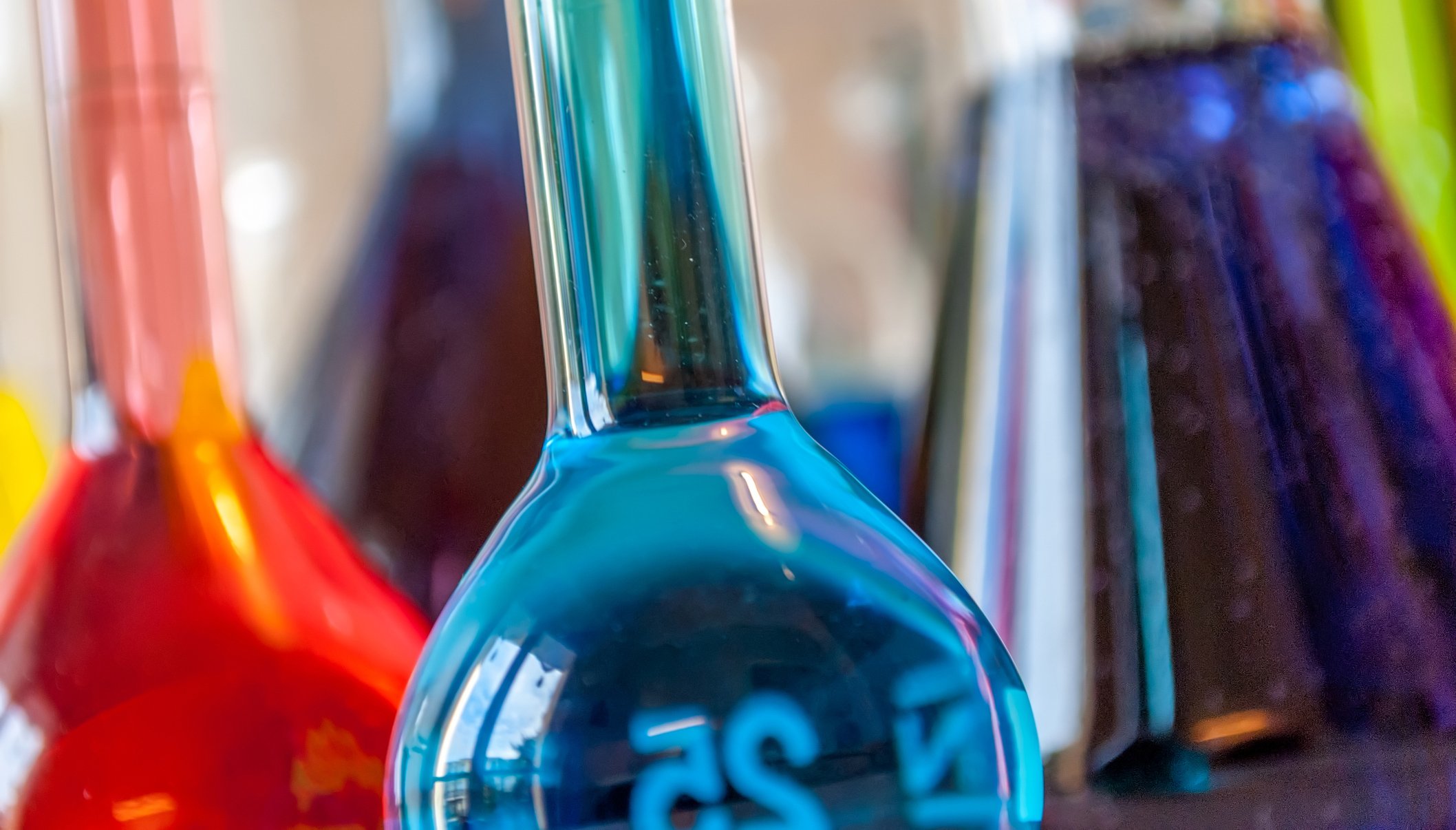 Blue liquid in a glass container with red liquid in a glass container in the background.